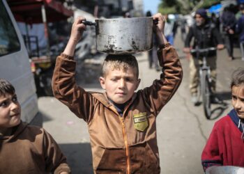 KANAK-kanak Palestin membawa periuk ketika berjalan ke arah tempat pengagihan makanan di Khan Younis di selatan Semenanjung Gaza.-AFP