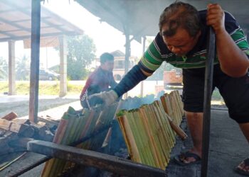 ISMAIL Bakar (kanan) membakar lemang yang ditempah pelanggannya di Kampung Sungai Rengas, Kuala Terengganu.  - UTUSAN/TENGKU DANISH BAHRI TENGKU YUSOFF