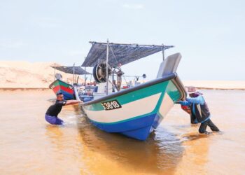 NELAYAN terpaksa menolak bot mereka yang tersangkut di beting pasir akibat muara cetek Sungai Merchang, Marang, Terengganu. - UTUSAN/PUQTRA HAIRRY ROSLI