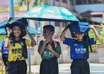 TIGA murid menutup kelapa mereka menggunakan beg dan payung berikutan cuaca panas di luar Sekolah Kebangsaan  Padang Mengkuang, Marang.- UTUSAN/PUQTRA HAIRRY ROSLI