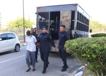 TERTUDUH diiringi oleh polis semasa menghadiri prosiding perbicaraan di Mahkamah Sesyen, Kota Bharu, Kelantan semalam. 
– UTUSAN/ROSLAWANI CHE SOH