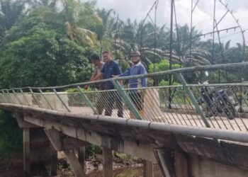 JOHARI Sarkom (tengah) Kemat Surono (kanan) menunjukkan tiang jambatan yang patah di Kampung Permatang Sepam Darat di Benut, Pontian.