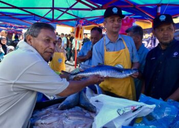 FAIZ Fadzil (tengah) memberikan ikan tenggiri yang dibeli pengguna pada  Program Jualan Agro Madani di Pasar Nelayan Pulau Gajah, Kota Bharu, Kelantan semalam.-MINGGUAN/ ROSLIZA MOHAMED