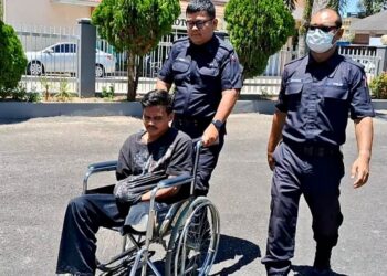 ANGGOTA polis menolak kerusi roda digunakan I Gede Purna Wijaya di Mahkamah Majistret Kemaman, hari ini. - UTUSAN/NIK NUR IZZATUL HAZWANI NIK ADNAN