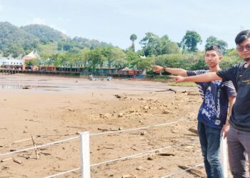 Dua pengunjung menunjukkan keadaan Tasik Kolam Bukit Merah yang kering berikutan musim panas ketika tinjauan di Bagan Serai semalam. – UTUSAN/WAT KAMAL ABAS