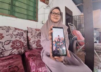 SITI Nurhidayah Abd. Ghani menunjukkan gambar kenangan keluarga bersama arwah suami di Kampung Merbau Berdarah, Sungai Panjang, Sabak Bernam semalam. – Utusan/ISKANDAR SHAH MOHAMED