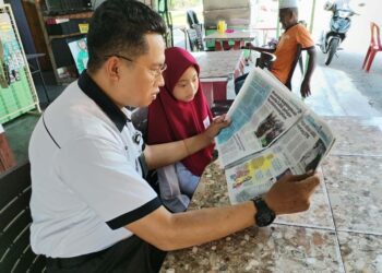 MOHD. Ridzuan Abu Samah dan anaknya, Nur Afifah Humairah melihat sisipan khas Utusan Pelajar di Taman Nirwana, Klebang, Melaka. – UTUSAN/AMRAN MULUP