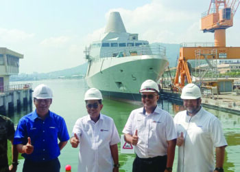 MOHAMED Khaled Nordin (tengah) menunjukkan isyarat bagus selepas meninjau proses pembinaan kapal tempur pesisir (di belakang) di Lumut Naval Shipyards Sdn. Bhd. di pangkalan Tentera Laut Diraja Malaysia (TLDM) di Lumut, semalam.