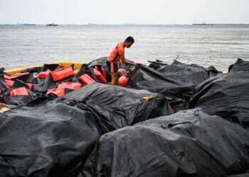 KAKITANGAN pengawal pantai menyusun penghadang terapung untuk digunakan mengawal tumpahan minyak di pelabuhan di Limay, Bataan.- AFP
