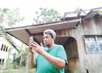 NAZIZ Abdul Zaman terpaksa keluar dari rumah untuk mencari talian telefon untuk berhubung di Kampung Kedai Lama, Rantau Panjang, Kelantan. – UTUSAN/YATIMIN ABDULLAH