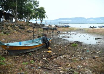 SEORANG nelayan, Zakaria Jusoh,66, terpaksa menolak botnya sejauh 200 meter ke tengah tasik sebelum dapat menghidupkan enjin berikutan empangan yang semakin menyusut sehingga paras 27.10 meter di Tasik Timah Tasoh, Padang Besar, Perlis semalam. – UTUSAN/IZLIZAN OTHMAN