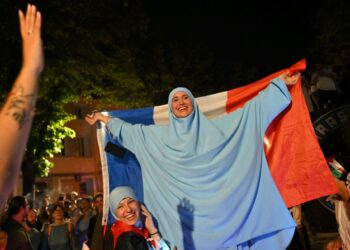 SEORANG wanita bertudung memegang bendera Perancis ketika orang ramai meraikan keputusan pertama pusingan kedua pilihan raya Parlimen di Marseille, pada Ahad.- AFP