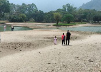 PENGUNJUNG berjalan di dasar Taman Tasik Taiping yang kering berikutan cuaca panas. – UTUSAN/WAT KAMAL ABAS