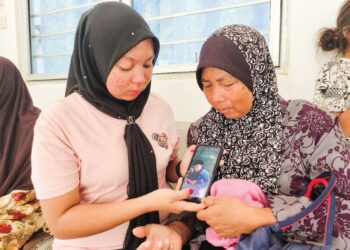 NUR Akma Aisyah Azizi (kiri) dan ibunya, Noraini Shaidan melihat gambar arwah Muhammad Izzham Hakimie yang lemas di Pantai Chenang, Langkawi, Kedah, kelmarin.