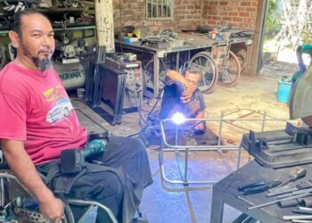 MOHD. Ariff Abdullah dan seorang  pembantunya yang juga OKU menyiapkan tempahan ubah suai motosikal roda tiga di bengkelnya di Alor Mengkudu, Alor Setar semalam. – UTUSAN/JAMLIAH ABDULLAH