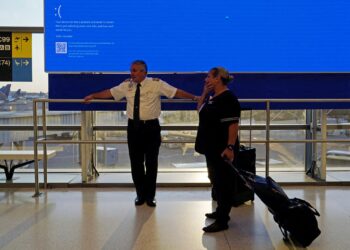 KAKITANGAN United Airlines berdiri di hadapan skrin berlepas yang mengalami gangguan kerana isu Blue Screen of Death (BSOD).- AGENSI