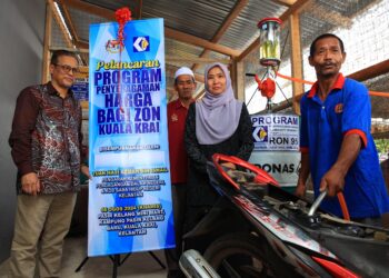 AZMAN Ismail (kiri) melihat penduduk mengisi bahan bakar petrol ke dalam motosikal sempena Program Penyeragaman Harga Bagi Zon Kuala Krai, hari ini-UTUSAN/KAMARUL BISMI KAMARUZAMAN.