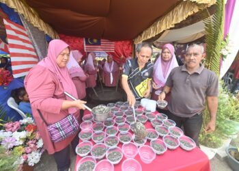 RAZAK Daud (tiga dari kanan) sedang mengisi bubur asyura di Felda Jengka 24 di Jerantut, Pahang. - FOTO/SHAIKH AHMAD RAZIF