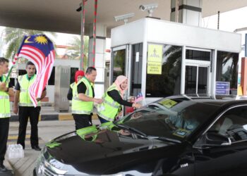 SUAIBAH Harun (kanan) memasang Jalur Gemilang di salah sebuah kenderaan 
di Plaza Tol Gemuruh, LPT2, di sini, hari ini. - UTUSAN/KAMALIZA KAMARUDDIN