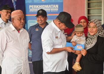 SAIFUDDIN Nasution Ismail (kiri) menyerahkan MyKid kepada seorang bayi, Muhammad Arash Muhammad Satria Agus bersama ibunya pada Program Menyemai Kasih Rakyat (MEKAR) Penyerahan Dokumen Pengenalan Diri di Kampung Baru Pulau Redang, Kuala Nerus, hari ini.- UTUSAN/PUQTRA HAIRRY ROSLI