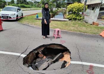 FAUZIAH Mohd. Kasim menunjukkan lubang besar akibat mendapan tanah di Jalan AP 21, Taman Alai Perdana, Melaka yang tiba-tiba terbentuk. – UTUSAN/AMRAN MULUP