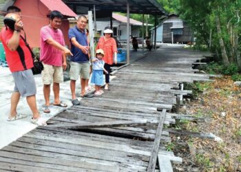 PENDUDUK menunjukkan  titi kayu yang reput dan merbahayakan  di Kampung Bagan Pasir Laut di Bagan Datuk semalam. – UTUSAN/AIN SAFRE BIDIN