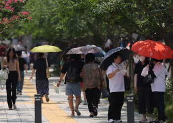 ORANG ramai yang berada berhampiran persimpangan Gwanghwamun di Seoul, menggunakan payung berikutan cuaca panas terik melanda seluruh negara.- AGENSI