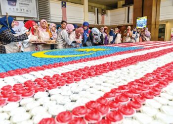 SUSYILA Mohd. Burhanuddin (lima dari kiri) membantu Ahli Lembaga Pengarah Yayasan Pahang, Datuk Seri Shahaniza Shamsuddin (enam dari kiri) menyiapkan Jalur Gemilang gergasi menggunakan kek cawan.