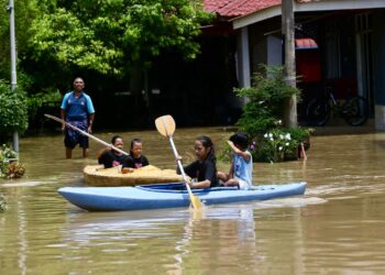 SEORANG penduduk mengawasi cucu-cucunya bermain kayak di hadapan rumah mereka yang dinaiki air di Kampung Titi Gajah, Alor Setar. - UTUSAN/ SHAHIR NOORDIN