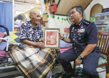 BESAR Long menunjukkan gambarnya semasa menjadi anggota Jungle Squad kepada Azli Mohd. Noor di Kampung Chabang Tiga, Kuala Terengganu, semalam. – UTUSAN/TENGKU DANISH BAHRI TENGKU YUSOFF