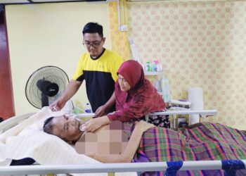 SHARINA Abd Razak (kanan) dibantu anaknya, Mohd. Sharil Kasim menjaga kebajikan Kasim Saad yang terlantar akibat penyakit angin ahmar di Felda Sungai Tekam Utara di Jerantut, Pahang. – UTUSAN/HARIS FADILAH AHMAD