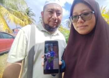 NUR Kamilah Ripin @ Arifin (kanan) dan suaminya, Muhammad Rajab menunjukkan gambar Ibrahim Adham Muhammad di Tanah Perkuburan Islam Kampung Sungai Renek, Besut, hari ini. - UTUSAN/WAN ZURATIKAH IFFAH WAN ZULKIFLI