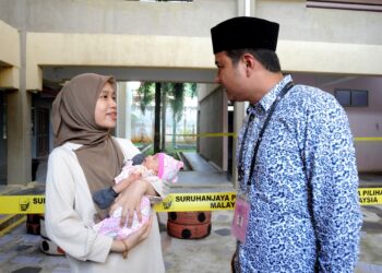 SYED HUSSIEN Syed Abdullah berbual dengan Nur Syafiqah Azani yang mendukung bayinya, Nur Syafaa Atiya  Mohd. Riyadh Irfan yang berumur sebulan ketika mengundi di SMK Seri Perdana, Kluang.