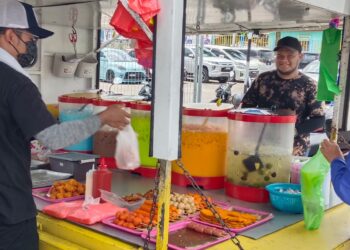 MUHAMMAD HAZIM Khalid melayan beberapa orang pengundu yang singgah membeli minuman dan makanan di gerainya di SK Kampung Melayu, Kluang.