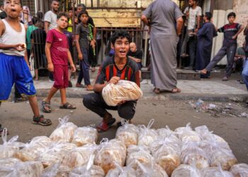 SEORANG budak Palestin menjual pek roti segar di sepanjang jalan pasar di Deir el-Balah, di tengah serangan tanpa henti Israel di Gaza.- AFP