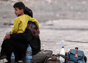 SEORANG wanita memangku anaknya berhampiran beg pakaian mereka di Jdeidat Yabus di sempadan Syria dengan Lubnan.-AFP