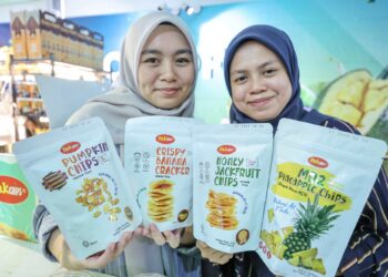 Pembantu jualan, Nik Fathiah Nasuha (kanan) dan Nurfazliyana Ahmad Farzeli menunjukkan produk makanan PakChips di Serdang semalam.