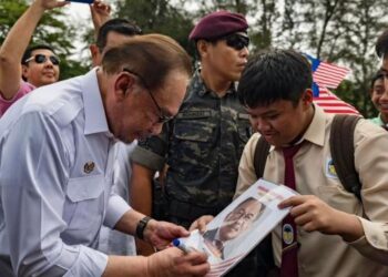 ANWAR Ibrahim menurunkan tandatangan pada poster yang tertera gambar beliau milik seorang pelajar sekolah yang hadir pada Majlis Santunan Budi, Tautan Kasih Felda Madani di Felda Sahabat, Lahad Datu, Sabah, hari ini. - FOTO/FACEBOOK PM