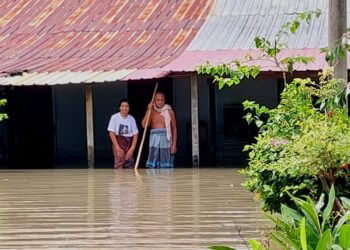 SITI Salmiah (kiri) dan Mohamad Ismail berdiri di hadapan rumah mereka yang masih digenangi air di Kampung Chegar, Tasek Gelugor, Pulau Pinang.