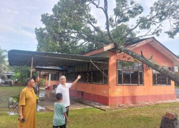 HANAFIAH Mat (kiri) meninjau keadaan sebuah balai raya yang dihempap pokok dalam kejadian ribut dan hujan lebat di Kampung Fikri, Chukai, Kemaman, Terengganu, hari ini.