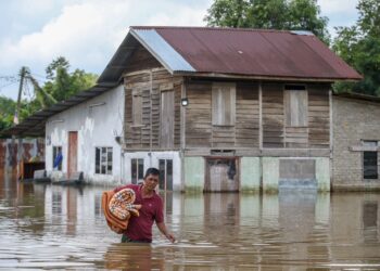 MOHAMAD Rosdi Said meredah banjir hampir separas pinggangnya untuk mengambil barangan di rumahnya yang masih digenangi air di Kampung Banggol Besi, Pendang. - UTUSAN/ SHAHIR NOORDIN