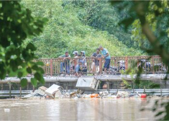 PENDUDUK membantu membersihkan barangan dihanyutkan banjir yang tersangkut pada sebuah jambatan di Kampung Alor Madi, Anak Bukit di Alor Setar. – UTUSAN/ SHAHIR NOORDIN