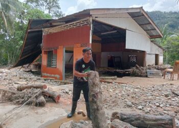 MOHD Naim Asri Baharom membuang kayu-kayu pokok yang hanyut ke dalam rumahnya yang roboh ketika banjir puing di Kampung Teluk Rambong, Baling.