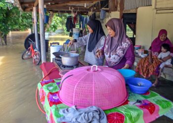 Kasma Ahmad (kanan) bersama anak dan cucunya memasak di luar rumahnya yang digenangi air akibat banjir di Kampung Kubang Betong, Changlun. - UTUSAN/SHAHIR NOORDIN