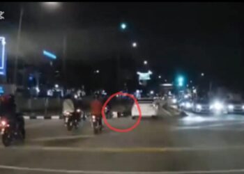 TANGKAP layar satu rakaman video yang tular menunjukkan sebuah kereta berwarna putih menghimpit sebuah motosikal (dalam bulatan merah) sehingga terjatuh di kawasan lampu isyarat berhampiran sebuah hospital swasta di Bayan Baru, Pulau Pinang