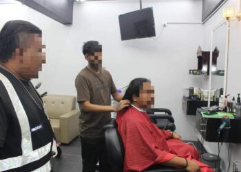 SEORANG pekerja warga asing (tengah) ditahan ketika sedang menggunting rambut pelanggannya dalam satu operasi penguatkuasaan di Pulau Pinang.