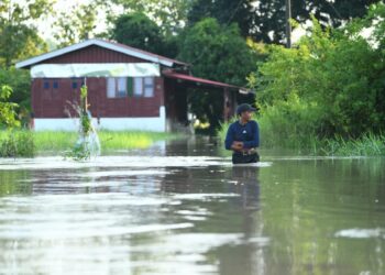 SEORANG penduduk meredah banjir untuk keluar dari rumahnya di Kampung Sungai Bakong, Arau, Perlis hari ini.-UTUSAN/IZLIZAN OTHMAN