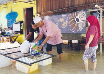 SHARMEELIANA Majid (kanan) menerima bantuan makanan berikutan rumahnya masih digenangi banjir sejak beberapa hari lalu di Kampung Padang Halban, Changlun, Kubang Pasu.