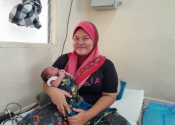 SITI ZULAIHA Abdullah memangku bayinya, Muhammad Ayden Aiys yang berusia dua minggu di PPS SK Seri Anom, Pontian.