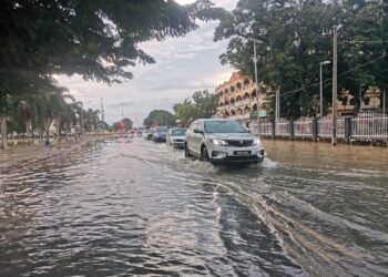 KENDERAAN melalui jalan yang dinaiki air akibat air pasang besar di bandar Teluk Intan hari ini. - UTUSAN/AIN SAFRE BIDIN